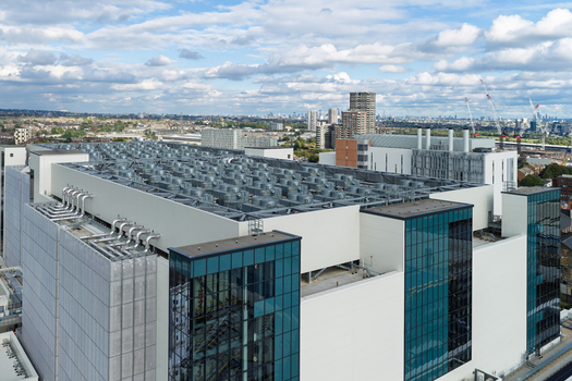 Aerial view of a modern data center with numerous cooling units on the roof and a glass and white panel facade in the United Kingdom. Aerial view of a modern data center with numerous cooling units on the roof and a glass and white panel facade in the United Kingdom.