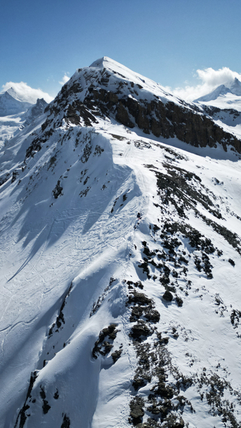 Aerial view of a snow covered mountain ridge under a clear blue sky the rugged terrain contrasting with the smooth snow Arete de sorebois Anniviers Valais Switzerland.