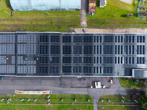 Aerial view of a large industrial building roof covered with solar panel arrays surrounded by green grass railway tracks and paved grounds in Olaine Olaine Municipality Latvia. Aerial view of a large industrial building roof covered with solar panel arrays surrounded by green grass railway tracks and paved grounds in Olaine Olaine Municipality Latvia.