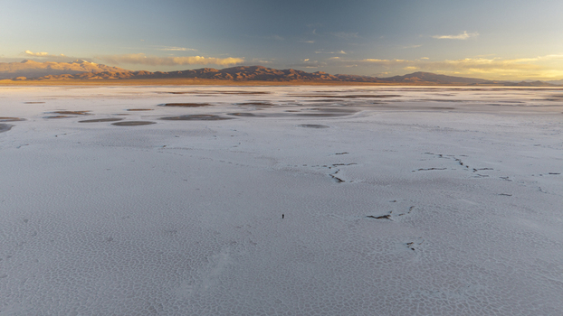 Aerial view of the vast white salt crust of Salinas Grandes with a lone person standing in the center under a golden sunset sky in La Poma Department Salta Province Argentina. Aerial view of the vast white salt crust of Salinas Grandes with a lone person standing in the center under a golden sunset sky in La Poma Department Salta Province Argentina.