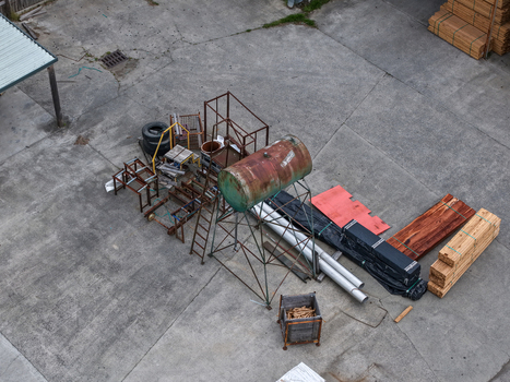 Melbourne Australia 25 September 2026 Aerial view of an industrial yard with a rusted tank on a frame timber stacks metal pipes and machinery parts on a concrete surface.