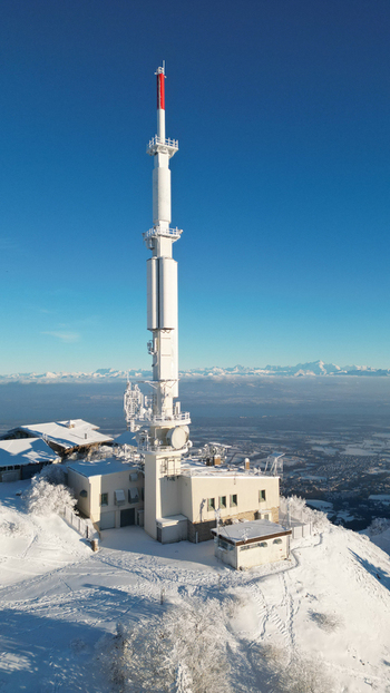 Aerial view of Col de la Faucille telecommunications tower surrounded by snow covered mountain landscape under a clear blue sky in Gex Auvergne Rhone Alpes France. Aerial view of Col de la Faucille telecommunications tower surrounded by snow covered mountain landscape under a clear blue sky in Gex Auvergne Rhone Alpes France.