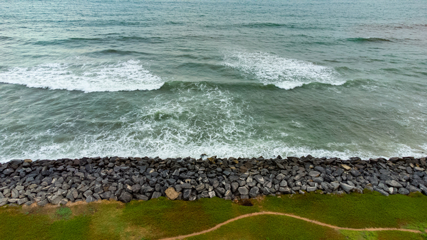 Aerial view of Accra Tema Beach Road featuring a rocky breakwater protecting the coastline from crashing waves with a grassy path alongside in Accra Greater Accra Region Ghana.