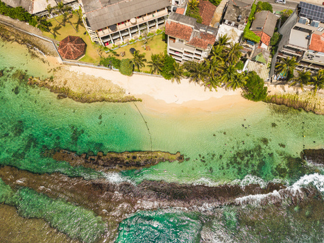 Aerial view of Thalpe Beach featuring turquoise waters rocky coral reefs and coastal resorts lined with palm trees in Talpe Southern Province Sri Lanka. Aerial view of Thalpe Beach featuring turquoise waters rocky coral reefs and coastal resorts lined with palm trees in Talpe Southern Province Sri Lanka.