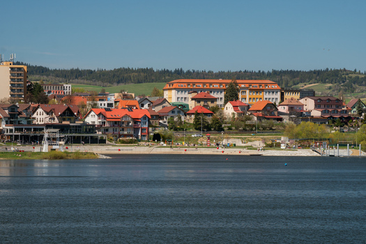 Aerial view of Namestovo town and Oravska priehrada dam featuring colorful buildings with red rooftops along the waterfront under a clear blue sky in Namestovo Zilina Region Slovakia. Aerial view of Namestovo town and Oravska priehrada dam featuring colorful buildings with red rooftops along the waterfront under a clear blue sky in Namestovo Zilina Region Slovakia.