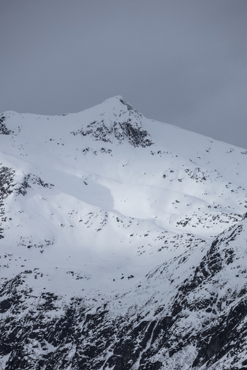 View of a majestic snow covered mountain peak with rocky slopes under an overcast winter sky in Ersfjord Troms Norway. View of a majestic snow covered mountain peak with rocky slopes under an overcast winter sky in Ersfjord Troms Norway.