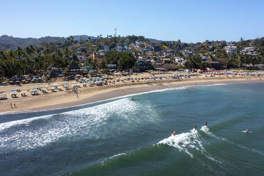 Aerial view of Sayulita beach with surfers riding waves sandy shore with umbrellas palm trees and coastal buildings in the background in Sayulita Nayarit Mexico. Aerial view of Sayulita beach with surfers riding waves sandy shore with umbrellas palm trees and coastal buildings in the background in Sayulita Nayarit Mexico.