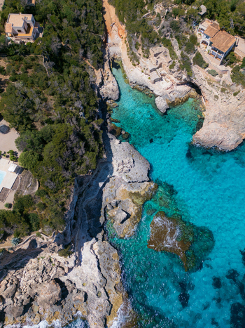 Aerial view of Cala Llombards cove featuring crystal clear turquoise water rugged limestone cliffs and Mediterranean vegetation with coastal villas Cala Llombards Illes Balears Spain. Aerial view of Cala Llombards cove featuring crystal clear turquoise water rugged limestone cliffs and Mediterranean vegetation with coastal villas Cala Llombards Illes Balears Spain.