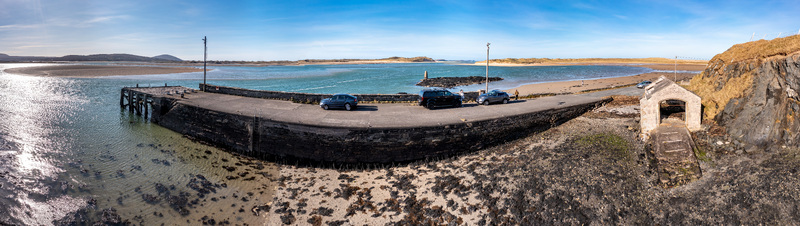 Aerial view of Ballyness Bay featuring a stone pier with parked cars sandy shores and calm turquoise waters under a clear blue sky in Ballyness County Donegal Ireland. Aerial view of Ballyness Bay featuring a stone pier with parked cars sandy shores and calm turquoise waters under a clear blue sky in Ballyness County Donegal Ireland.
