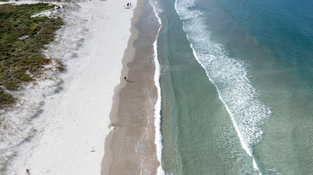 Aerial view of Omaha Beach with white sand turquoise waves and dunes in Omaha Auckland New Zealand.