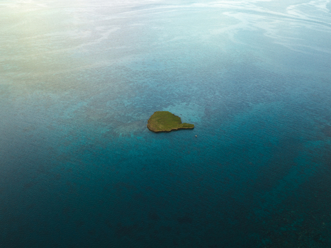 Aerial view of a small island surrounded by the turquoise and deep blue ocean glistening under the sun Noumea New Caledonia. Aerial view of a small island surrounded by the turquoise and deep blue ocean glistening under the sun Noumea New Caledonia.