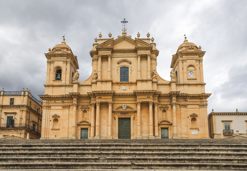View of the Noto Cathedral with its Baroque facade and grand stone staircase under an overcast sky in Noto Sicily Italy. View of the Noto Cathedral with its Baroque facade and grand stone staircase under an overcast sky in Noto Sicily Italy.