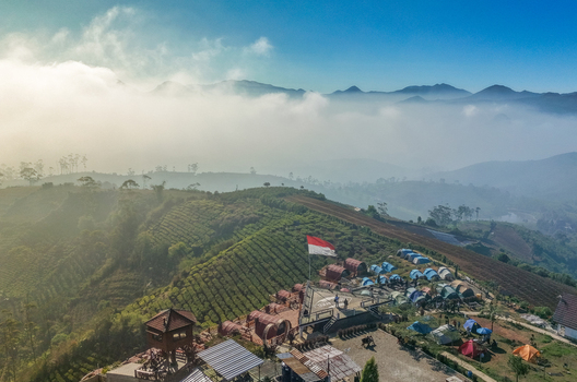 Aerial view of Sunrise Point Cukul with a camping area tents and an Indonesian flag overlooking lush tea plantations and misty mountains in Kecamatan Pangalengan Jawa Barat Indonesia. Aerial view of Sunrise Point Cukul with a camping area tents and an Indonesian flag overlooking lush tea plantations and misty mountains in Kecamatan Pangalengan Jawa Barat Indonesia.