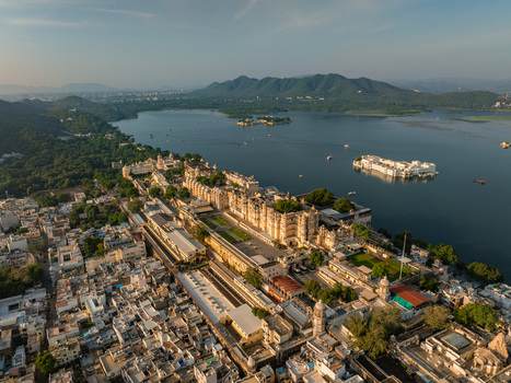 Aerial view of the historic City Palace complex situated on the banks of Lake Pichola featuring intricate architecture courtyards and surrounding urban rooftops in Udaipur Rajasthan India.