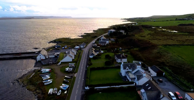 Aerial view of Bruichladdich village with its coastal road small harbor with boats and surrounding green fields in Bruichladdich Scotland United Kingdom.