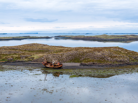 Aerial view of a rusted shipwreck resting on a rocky mossy shoreline surrounded by calm coastal waters in Iceland. Aerial view of a rusted shipwreck resting on a rocky mossy shoreline surrounded by calm coastal waters in Iceland.