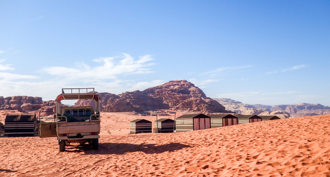View of a 4x4 vehicle parked near traditional Bedouin tents in the vast red sand dunes of the Wadi Rum Desert under a clear blue sky in Wadi Rum Village Aqaba Governorate Jordan. View of a 4x4 vehicle parked near traditional Bedouin tents in the vast red sand dunes of the Wadi Rum Desert under a clear blue sky in Wadi Rum Village Aqaba Governorate Jordan.