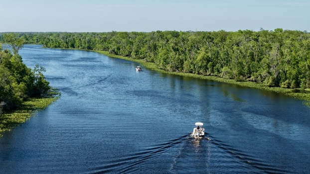 Aerial view of Sixmile Creek with motorboats cruising on the blue water surrounded by lush green cypress trees and forest St. Johns County Florida United States.