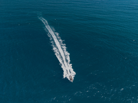 Aerial view of a motorboat cruising through the deep blue waters of the Pacific Ocean leaving a long white wake behind it near Long Reef Headland Collaroy New South Wales Australia.