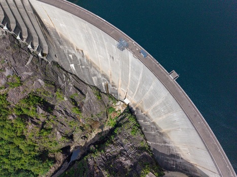 Aerial view of the Verzasca Dam showing its massive concrete wall curving between rocky cliffs and deep blue water in Gordola Ticino Switzerland. Aerial view of the Verzasca Dam showing its massive concrete wall curving between rocky cliffs and deep blue water in Gordola Ticino Switzerland.