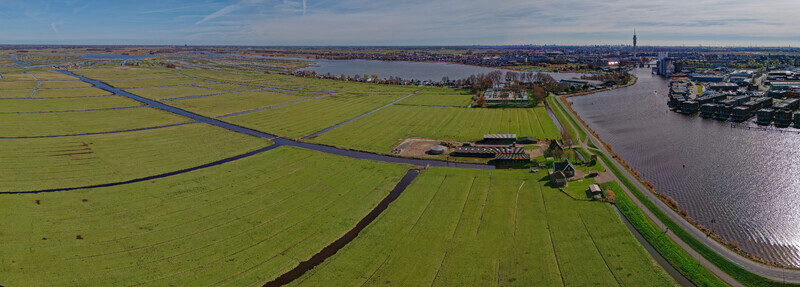 Aerial view of lush green fields cut by dark canals meet modern architecture across the shimmering water Wormer Netherlands. Aerial view of lush green fields cut by dark canals meet modern architecture across the shimmering water Wormer Netherlands.