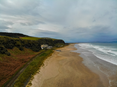 Aerial view of the sandy coastline and cliffs at Downhill Beach with a railway line along the grassy hills under a cloudy sky in Coleraine Northern Ireland United Kingdom. Aerial view of the sandy coastline and cliffs at Downhill Beach with a railway line along the grassy hills under a cloudy sky in Coleraine Northern Ireland United Kingdom.