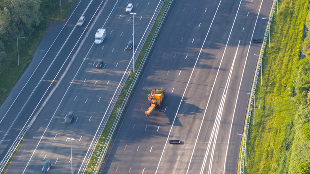 Waardenburg Netherlands 09 May 2026 Aerial view of a multi lane highway with a yellow road maintenance vehicle and cars driving past green embankments. Waardenburg Netherlands 09 May 2026 Aerial view of a multi lane highway with a yellow road maintenance vehicle and cars driving past green embankments.