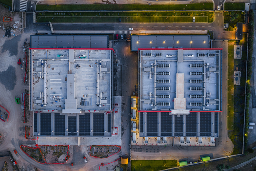 Aerial view of a modern datacenter facility featuring two large industrial buildings with rooftop HVAC units and solar panels in Settecamini Lazio Italy.