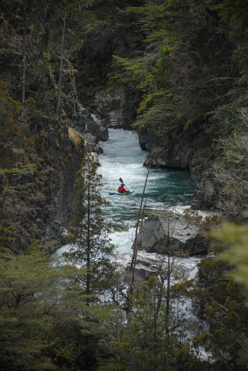 View of a kayaker paddling through the turquoise rapids of the Rio Manso canyon surrounded by dense green forest San Carlos de Bariloche Rio Negro Argentina. View of a kayaker paddling through the turquoise rapids of the Rio Manso canyon surrounded by dense green forest San Carlos de Bariloche Rio Negro Argentina.