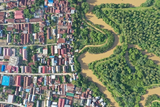 Aerial view of Pulau Maginti showing the dense residential area with traditional rooftops adjacent to a winding river and lush tropical vegetation in Maginti South East Sulawesi Indonesia.