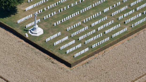 Aerial view of Delville Wood Cemetery with rows of white headstones and a Cross of Sacrifice surrounded by agricultural fields in Longueval Hauts de France France.