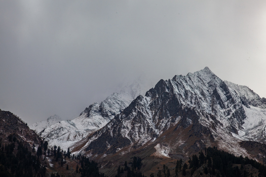View of the snow capped peaks of Naltar Valley with rugged slopes and evergreen trees under a cloudy sky Naltar Valley Gilgit Pakistan. View of the snow capped peaks of Naltar Valley with rugged slopes and evergreen trees under a cloudy sky Naltar Valley Gilgit Pakistan.