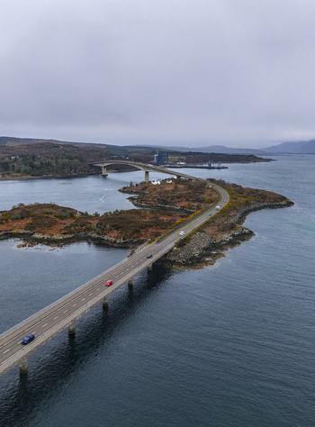 Aerial view of Skye Bridge spanning across the sea with cars driving along the road under an overcast sky Isle of Skye Scotland United Kingdom.
