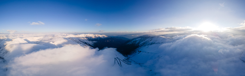 Aerial view of Babusar Pass winding through snow covered mountain peaks under a bright sun and thick clouds Babusar KPK Pakistan.