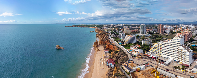 Aerial view of the golden cliffs and sandy shores of Praia da Rocha beach with modern high rise buildings along the coastline in Portimao Faro District Portugal.