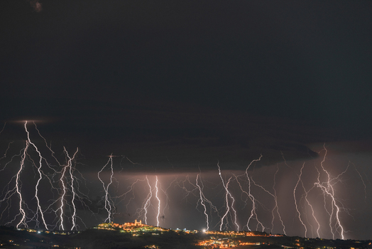 View of multiple lightning strikes illuminating the night sky over the historic town of Montecosaro Marche Italy. View of multiple lightning strikes illuminating the night sky over the historic town of Montecosaro Marche Italy.