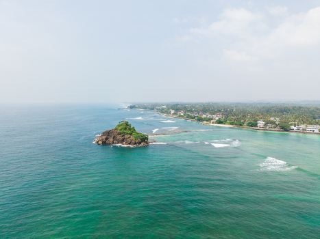 Aerial view of Devil s Rock a small rocky islet with lush greenery surrounded by turquoise ocean waves along the tropical coastline Ahangama Southern Province Sri Lanka. Aerial view of Devil s Rock a small rocky islet with lush greenery surrounded by turquoise ocean waves along the tropical coastline Ahangama Southern Province Sri Lanka.