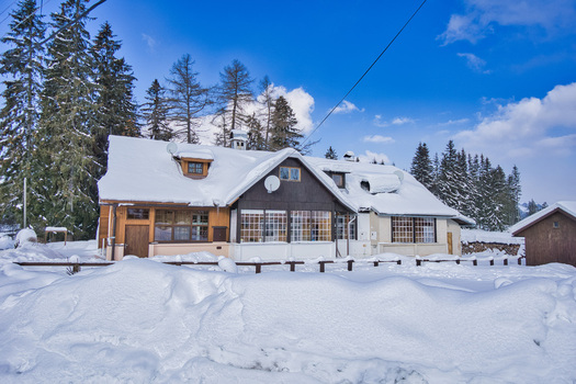 View of a snow covered building with a dark roof stands nestled among evergreen trees under a bright blue sky with scattered clouds Donovaly Banskobystricky kraj Slovakia. View of a snow covered building with a dark roof stands nestled among evergreen trees under a bright blue sky with scattered clouds Donovaly Banskobystricky kraj Slovakia.