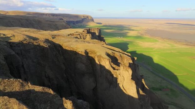 Aerial view of dramatic cliffs and green fields in Iceland.