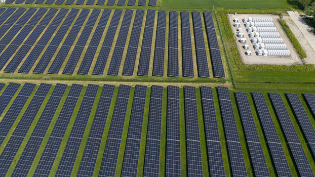 Aerial view of rows of solar panels in a large solar farm with battery storage units and green fields in Wanneperveen Overijssel Netherlands. Aerial view of rows of solar panels in a large solar farm with battery storage units and green fields in Wanneperveen Overijssel Netherlands.