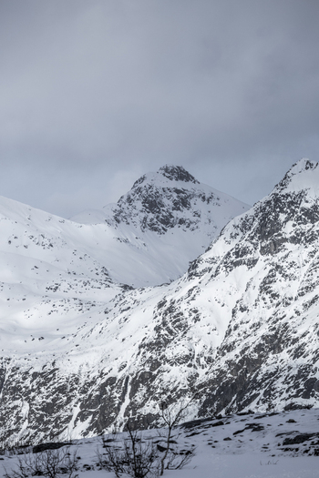 View of snow covered mountain peaks and jagged rocky slopes under an overcast winter sky in Ersfjord Troms Norway. View of snow covered mountain peaks and jagged rocky slopes under an overcast winter sky in Ersfjord Troms Norway.