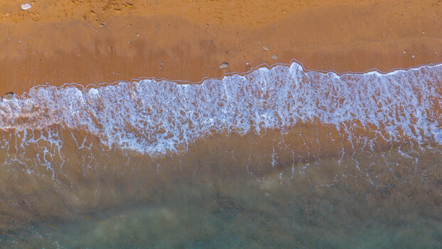 Aerial view of golden sand and white sea foam waves washing onto the shore at West Bay England United Kingdom. Aerial view of golden sand and white sea foam waves washing onto the shore at West Bay England United Kingdom.