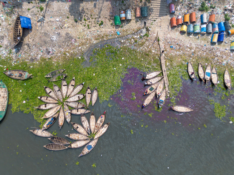 Aerial view of wooden boats arranged in flower patterns on the Buriganga River with colorful barrels and green water hyacinths along the shore in Dhaka Dhaka Division Bangladesh.