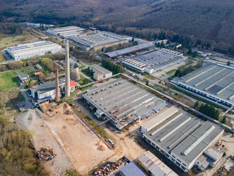 Aerial view of industrial buildings with red brick chimney stacks piercing the skyline contrasting with the green trees Detva Banskobystricky kraj Slovakia. Aerial view of industrial buildings with red brick chimney stacks piercing the skyline contrasting with the green trees Detva Banskobystricky kraj Slovakia.