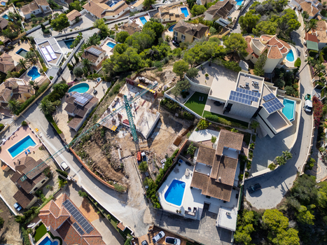 Aerial view of a construction site with a crane surrounded by residential villas with swimming pools and solar panels in Moraira Valencian Community Spain.