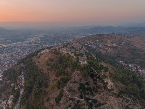 Aerial view of the historic Berat Castle fortress ruins situated on a hilltop overlooking the city with pine trees and sunset light in Berat Berat County Albania. Aerial view of the historic Berat Castle fortress ruins situated on a hilltop overlooking the city with pine trees and sunset light in Berat Berat County Albania.