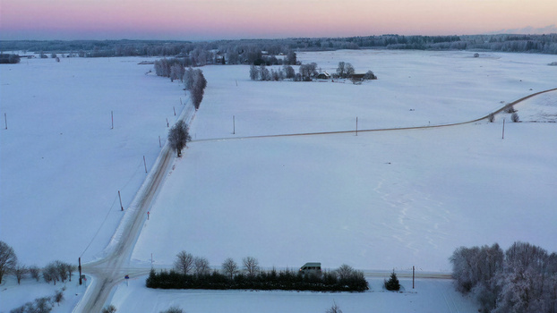 Aerial view of a snow covered rural landscape with a road intersection frost covered trees and a small vehicle parked near a line of pine trees in Latvia. Aerial view of a snow covered rural landscape with a road intersection frost covered trees and a small vehicle parked near a line of pine trees in Latvia.