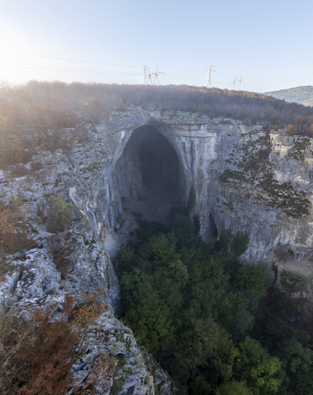 Aerial view of the massive entrance of Prohodna Cave surrounded by limestone cliffs and autumn forest in Karlukovo Lovech Bulgaria. Aerial view of the massive entrance of Prohodna Cave surrounded by limestone cliffs and autumn forest in Karlukovo Lovech Bulgaria.