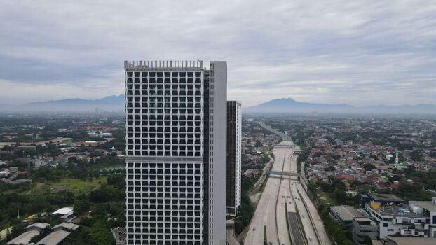 Aerial view of a modern high rise building with a grid facade next to the Jalan Tol Depok Antasari highway with urban sprawl in Kecamatan Cilandak Daerah Khusus Ibukota Indonesia. Aerial view of a modern high rise building with a grid facade next to the Jalan Tol Depok Antasari highway with urban sprawl in Kecamatan Cilandak Daerah Khusus Ibukota Indonesia.