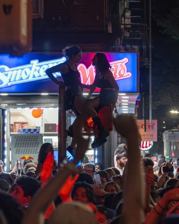 Williamsburg New York USA 14 June 2026 View of two women sitting on a traffic light pole amidst a cheering crowd during a street celebration. Williamsburg New York USA 14 June 2026 View of two women sitting on a traffic light pole amidst a cheering crowd during a street celebration.